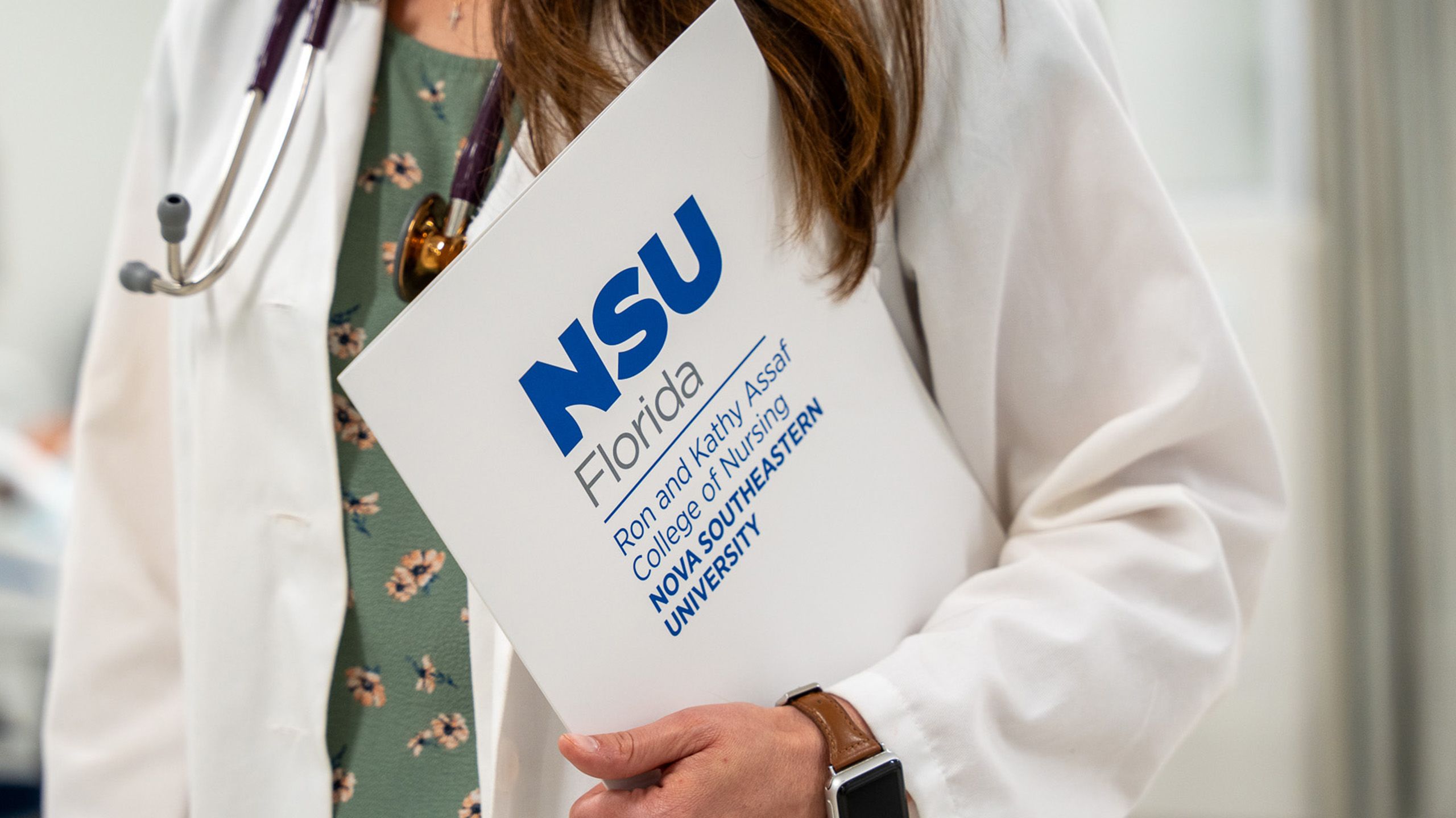 close up of professor holding a folder with the NSU Florida Ron and Kathy Assaf College of Nursing logo